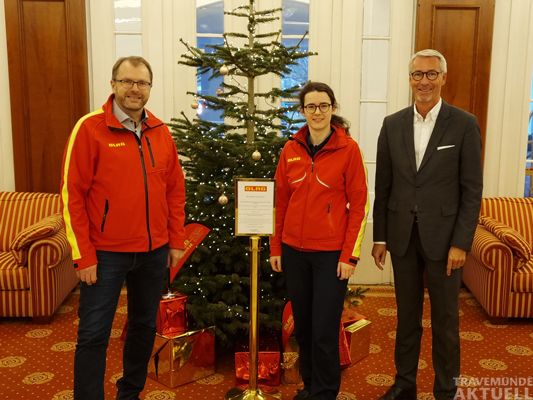 Thomas Becker (Vorsitzender der DLRG Lübeck e.V.), Carlotta Derad (Verbandskommunikations-Chefin des DLRG Lübeck e.V.) und Kay Plesse (Hoteldirektor Atlantic Grand Hotel Travemünde) vor dem Wunsch-Weihnachtsbaum. – Foto: Veranstalter