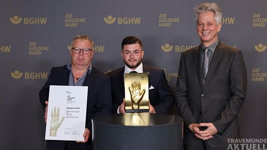 Bild, v. li.: Jörg Eilers (Fachkraft für Arbeitssicherheit der LHG) und Jastin Dos Santos Costa freuen sich über die Auszeichnung, die ihnen John Bötticher, Mitglied Jury und Vorstand BGHW, überreicht hat. Foto Bauer/BGHW